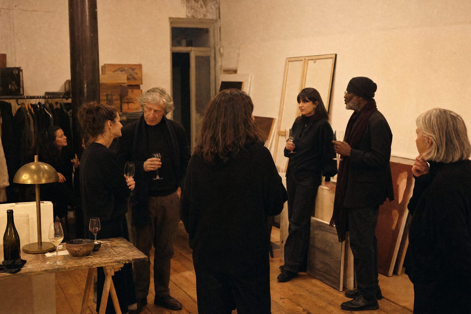 A gallery back room after an opening, a few people in conversation among leaning canvases